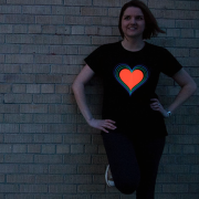 Girl leaning against brick wall in dark wearing a fully illuminated rainbow Heart LED T-shirt design