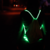 Someone walking down dark street wearing a green illuminated LED drawstring bag