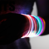 Extra close up of Someone wearing 7 different LED bracelets on their arm, all lighting up in different colors