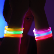 Girl in dark room holding up arms in front of face to show LED bracelets on wrist lighting up in many different colors