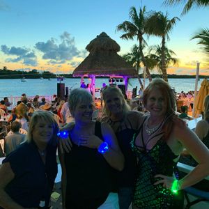 Four women wearing different colored LED bracelets lighting up in front of stage at concert on the water
