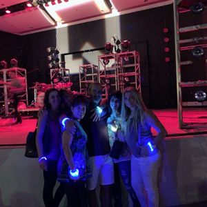 Group of women and men wearing light up LED bracelets in front of stage in dark concert