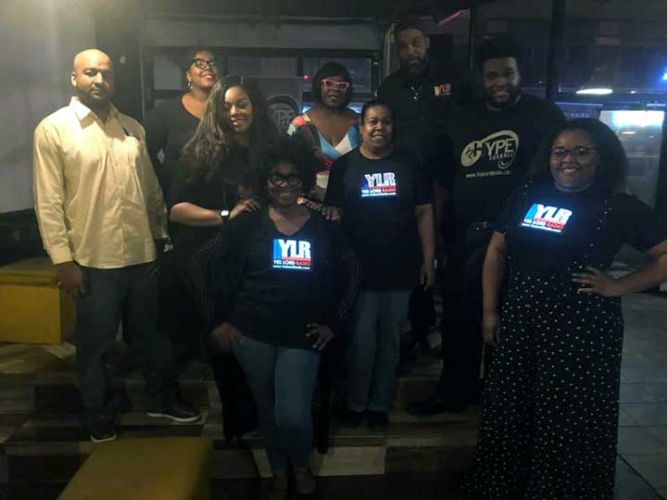 Group of African Americans wearing light up shirts in dark studio setting with logo glowing