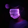 Person in dark room wearing brightly lit LED mask glowing bright purple and reflecting off her hat
