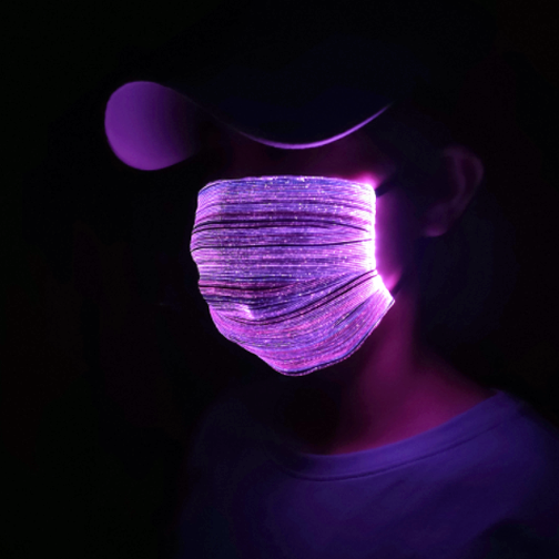 Person in dark room wearing brightly lit LED mask glowing bright purple and reflecting off her hat