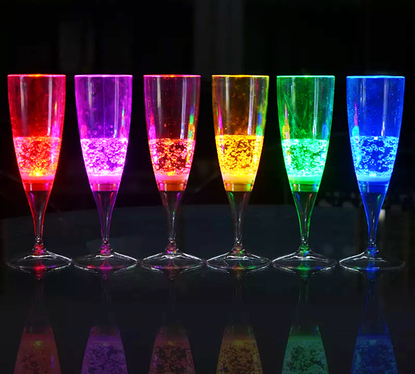 6 pack of LED champagne flutes in a line glowing bright red, pink, orange, yellow, green, and blue in a dark room