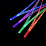 Carnival logo laser engraved onto bright neon LED lanyards shining red, green, purple and blue on four different lanyards in a dark room