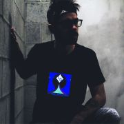 Man kneeling leaning against cinder block wall in dark basement while light up t-shirt design illuminates the room
