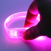 Thumb pressing button on battery pack of custom LED bracelet to turn it on and off, currently glowing hot pink