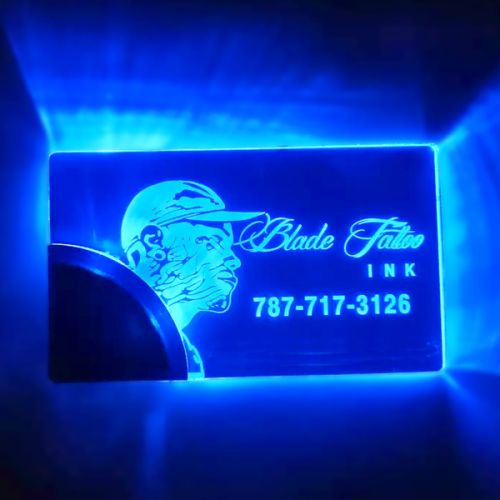 Laser engraved portrait of man with Blade Tattoo Ink and phone number on custom LED business card glowing bright blue
