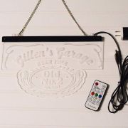 Clear acrylic LED sign turned off with laser engraved logo very faintly visible showing metal hanging chain, plug, and remote control