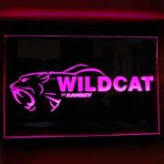 Wildcat text and logo laser engraved onto neon acrylic sign lighting up bright pink in dark room