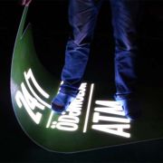 Person standing on glowing sign that they are also holding in their hand to show the flexibility and durability of the material