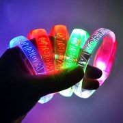 Hand holding five different colored custom LED bracelets lighting up bright neon colors