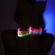 Person holding hands in front of face showing six different colored custom LED bracelets lighting up pink, orange, green, red, blue and yellow