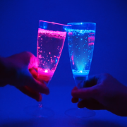 Pink and Blue LED champagne glass clinging together in cheers motion in dark room
