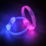 Two bracelets with custom engraved Muster logo lighting up bright blue and hot pink in dark room