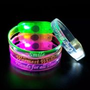 Three custom LED bracelets stacked up with another white LED bracelet leaning against it in a dark room, all shining brightly