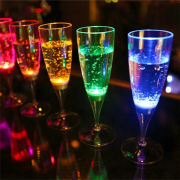 Five LED champagne glasses lighting up bright rainbow colors, with blue and green in the foreground and yellow orange and red in the background illuminating brightly on dark bar