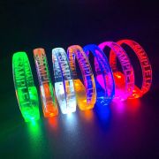 Seven custom LED bracelets with sample logo laser engraved lined up in a row showing each color, green, orange, white, yellow, blue, pink and red