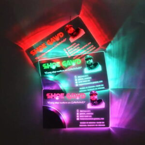 Three LED business cards stacked in dark room showing different color LEDs lighting up UV printed design for shoe company with contact information and pictures glowing brightly