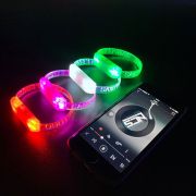 Four different colored custom LED bracelets lined up in a row next to phone playing music to show they are sound activated