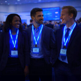 Three professionals at a conference wearing blue LED light-up lanyards while smiling and interacting in a dimly lit event setting