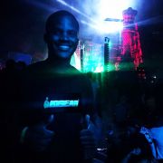 Man smiling with two thumbs up wearing custom company light up t-shirt illuminating brightly in festival setting