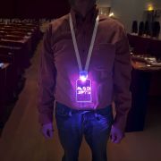 A man showcases a lanyard with an illuminating badge branded with a logo for Mad Arts