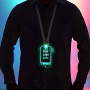 Silhouette of man in button down shirt from the neck down wearing a glowing LED ID badge around their neck which shines bright green in a dark setting