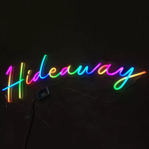 LED neon sign reading "Hideaway" lighting up in a gradient of rainbow colors with each letter containing multiple neon yellow, blue, pink, green, and red