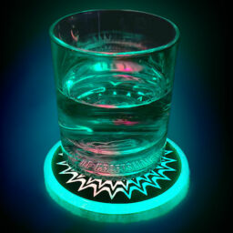 Picture of glass of water on LED drink coaster which is glowing bright green and making the drink glow as well