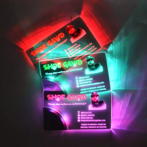 Three LED business cards stacked in dark room showing different color LEDs lighting up UV printed design for shoe company with contact information and pictures glowing brightly
