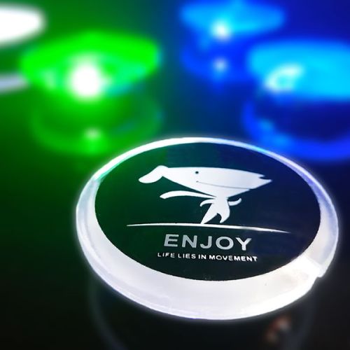 Close up of custom LED pin with "Enjoy" and cartoon logo lighting up bright white with blue and green LED pins lighting up in the background