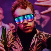 redheaded guy at party holding beer and wearing LED sunglasses shutter shades lighting up fully while people dance in the background