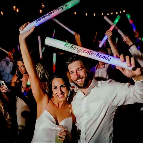 Happy couple at wedding dancing with guests waving color changing LED foam sticks in the air