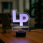 Professional LED acrylic branding display with the Lindner Properties logo glowing in purple on an office desktop