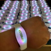 Close up of hand wearing illuminated LED wristband with "Ophelia" custom print, in front of several other glowing bracelets