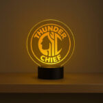 Custom round acrylic LED sign with engraved ‘Thunder Chief’ logo glowing in warm yellow on a shelf