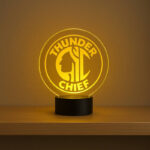 Custom round acrylic LED sign with engraved ‘Thunder Chief’ logo glowing in warm yellow on a shelf