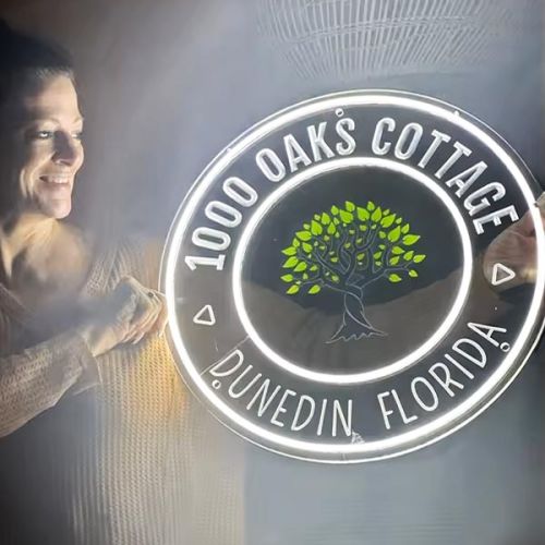 smiling woman holding custom LED neon sign with business logo and location brightly illuminating