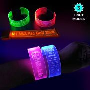 close up of wrist wearing two large glowing bracelets with engraved designs in front of other custom LED wristbands in neon colors