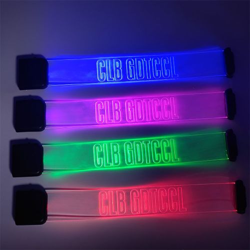 Four laser engraved LED wristbands laid open on a table each lighting up a different color from top to bottom: blue, hot pink, lime green, and red