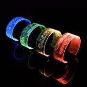 Four custom engraved LED bracelet designs lined up on a dark table each glowing a bright neon color
