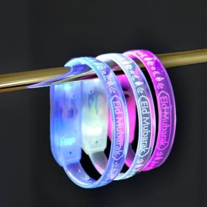three Eid Mubarek custom engraved LED bracelets on display rack glowing bright blue, white and pink