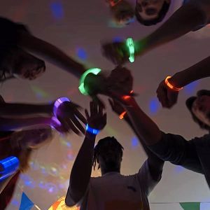 Group of people wearing illuminated bracelets putting their hands together in center while dancing