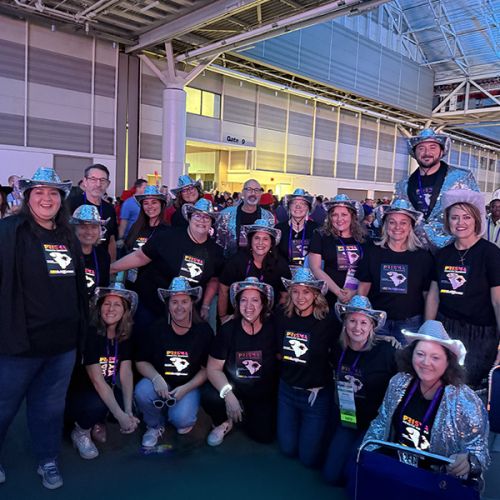 Large group of people wearing rhinestone cowboy hats posing with their light up shirts at a conference