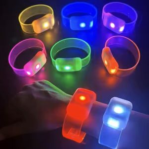 close up of wrist wearing two different LED wristbands glowing red and white, in front of 6 other LED wristbands on table each glowing a different rainbow color