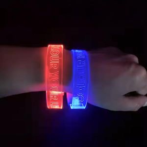 close up of wrist in dark room wearing two different color LED wristbands with "colour your world" laser engraved onto each