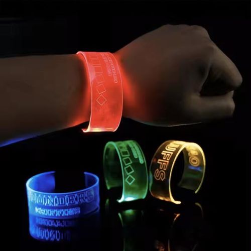 Close up of wrist wearing XL wristband in front of three other LED wristbands that are clasped on a dark table below